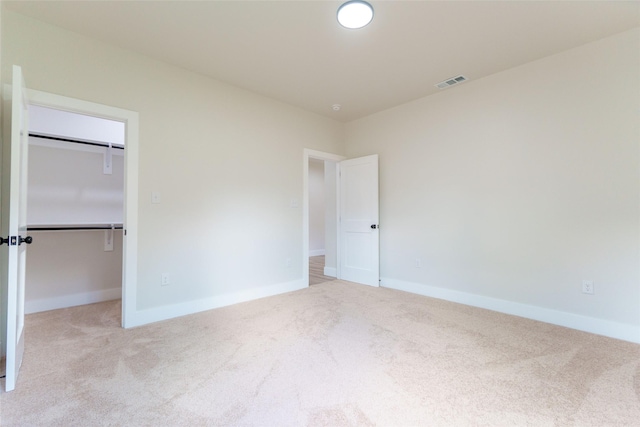 unfurnished bedroom featuring a walk in closet, a closet, and light carpet