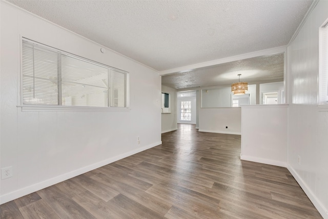 empty room featuring a textured ceiling, baseboards, wood finished floors, and ornamental molding