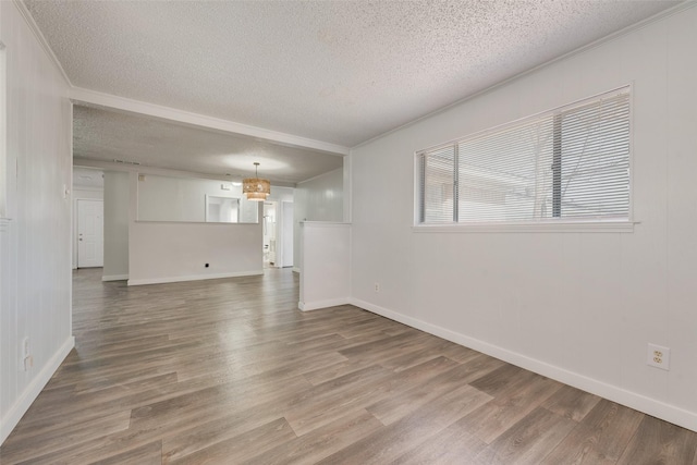 unfurnished room with baseboards, a textured ceiling, ornamental molding, and wood finished floors