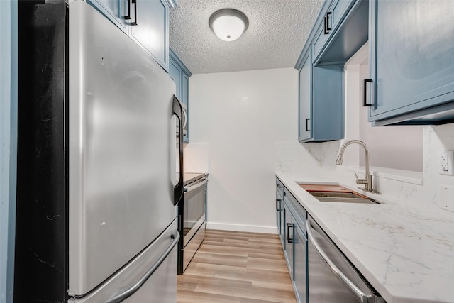 kitchen featuring a textured ceiling, a sink, blue cabinetry, appliances with stainless steel finishes, and light wood finished floors