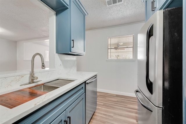 kitchen featuring light stone counters, appliances with stainless steel finishes, light wood-style flooring, and visible vents