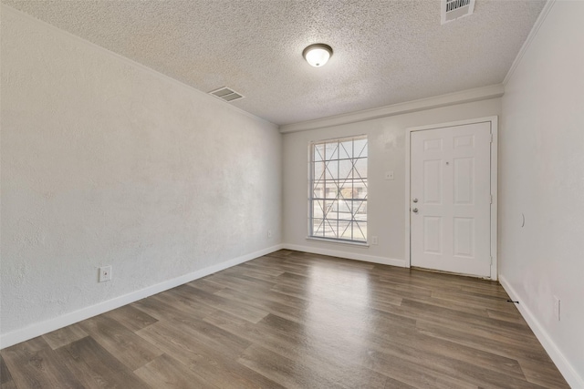 empty room with visible vents, crown molding, baseboards, and wood finished floors