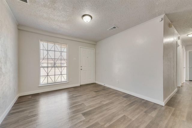 empty room with wood finished floors, visible vents, and crown molding