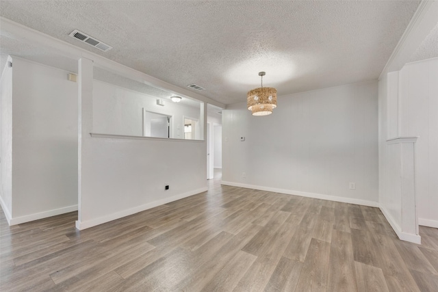 empty room with a textured ceiling, wood finished floors, visible vents, and a notable chandelier