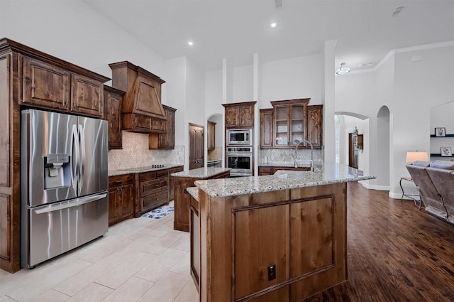 kitchen with light stone counters, stainless steel appliances, an island with sink, and a high ceiling