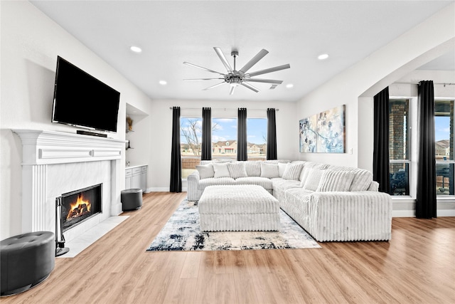 living room featuring built in shelves, a tile fireplace, ceiling fan, and light wood-type flooring