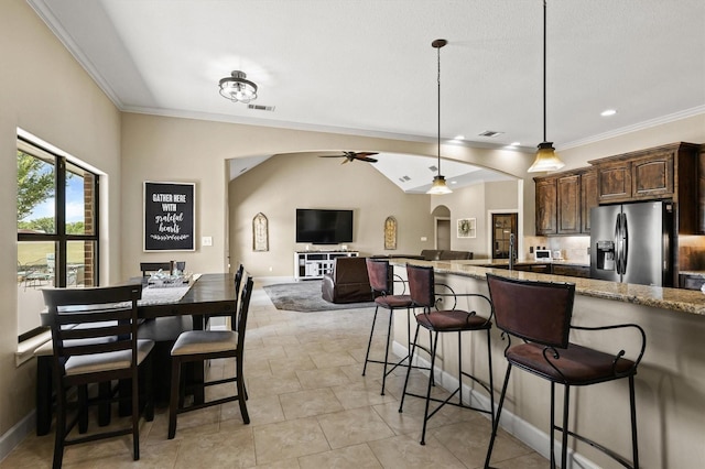kitchen featuring a kitchen bar, dark brown cabinets, ornamental molding, stainless steel refrigerator with ice dispenser, and light stone counters