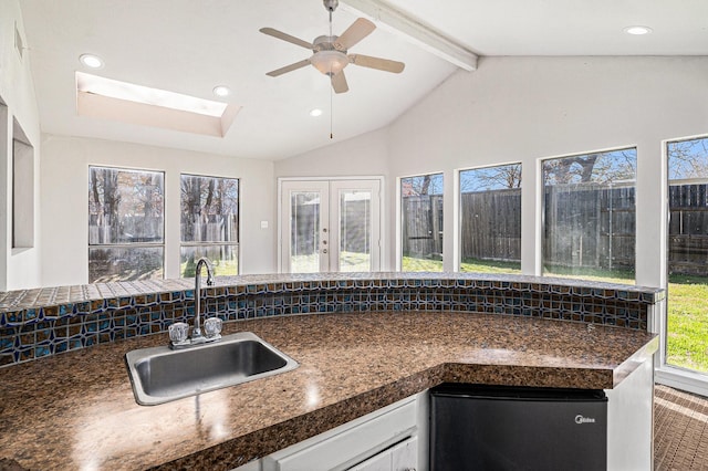 kitchen with sink, stainless steel fridge, white cabinetry, lofted ceiling with beams, and french doors