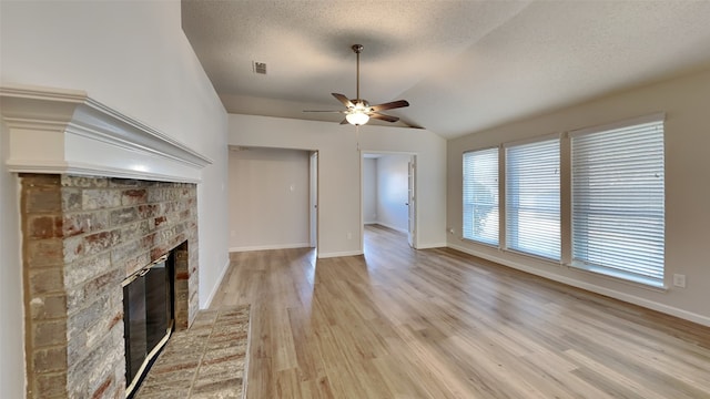 unfurnished living room featuring vaulted ceiling, a textured ceiling, light wood-type flooring, ceiling fan, and a fireplace