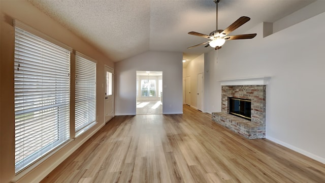 unfurnished living room featuring a stone fireplace, vaulted ceiling, a textured ceiling, light wood-type flooring, and ceiling fan