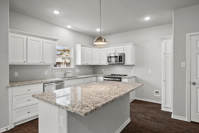 kitchen with sink, light stone counters, a kitchen island, stainless steel appliances, and white cabinets