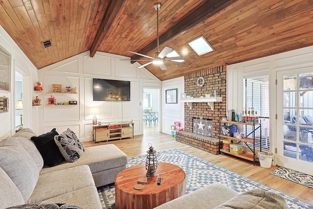 living room featuring ceiling fan, lofted ceiling with beams, light hardwood / wood-style floors, a brick fireplace, and wooden ceiling