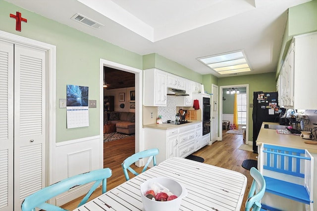 kitchen with white cabinetry, wood-type flooring, black appliances, and tasteful backsplash