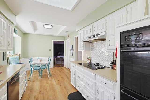 kitchen with white cabinets, decorative backsplash, black appliances, a raised ceiling, and light hardwood / wood-style flooring