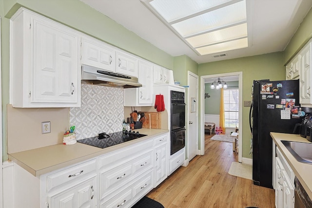 kitchen with tasteful backsplash, white cabinets, a notable chandelier, black appliances, and light wood-type flooring