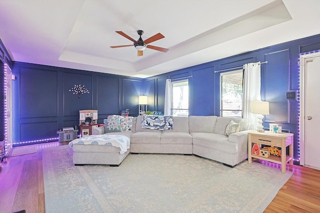 living room featuring hardwood / wood-style flooring, a raised ceiling, and ceiling fan