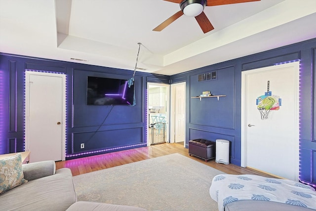 living room featuring a raised ceiling, wood-type flooring, and ceiling fan