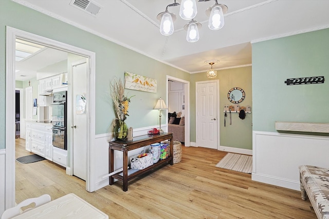 foyer entrance featuring crown molding, a chandelier, and light hardwood / wood-style flooring