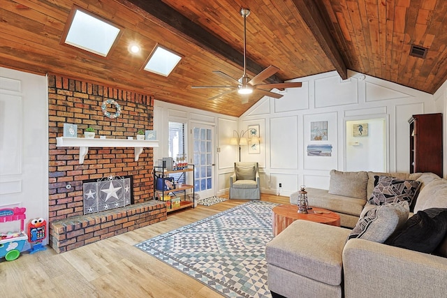 living room featuring ceiling fan, vaulted ceiling with skylight, wood-type flooring, a brick fireplace, and wooden ceiling