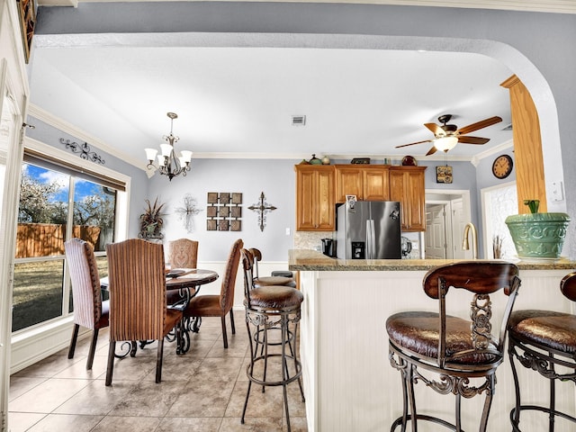 kitchen featuring a breakfast bar area, crown molding, stainless steel fridge, kitchen peninsula, and ceiling fan with notable chandelier