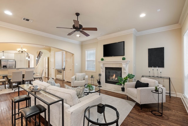 living room with crown molding, ceiling fan with notable chandelier, a fireplace, and dark hardwood / wood-style flooring