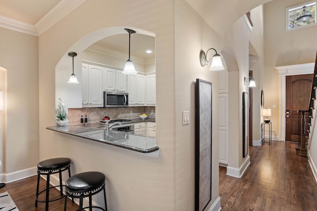 kitchen featuring white cabinets, backsplash, dark stone counters, kitchen peninsula, and crown molding