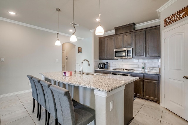 kitchen with dark brown cabinetry, sink, a center island with sink, pendant lighting, and stainless steel appliances