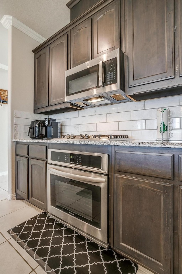 kitchen featuring light tile patterned floors, crown molding, appliances with stainless steel finishes, dark brown cabinets, and decorative backsplash