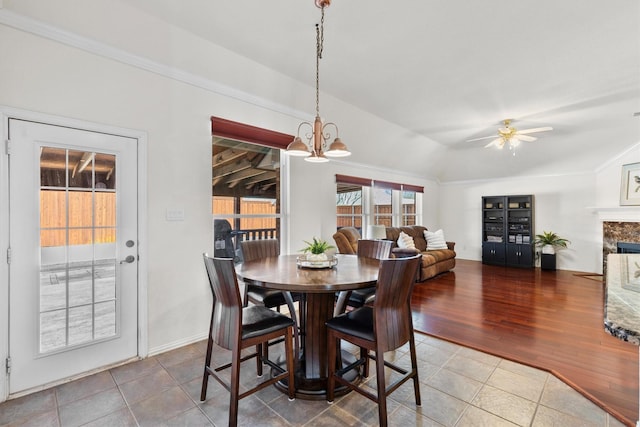 dining area with ceiling fan with notable chandelier, a fireplace, lofted ceiling, and wood finished floors