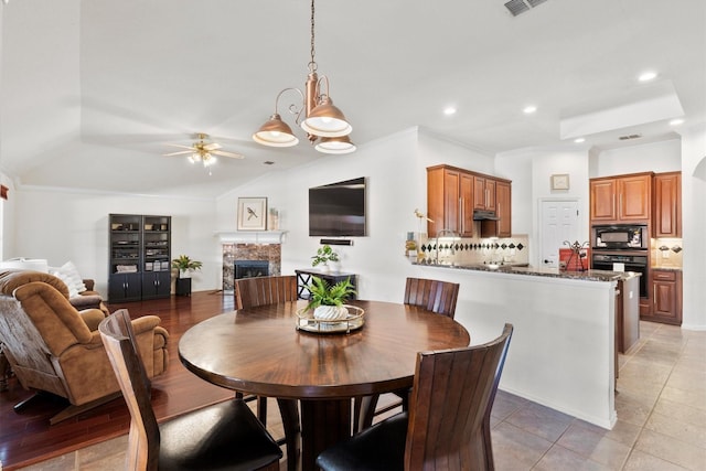 dining area with crown molding, ceiling fan, tile patterned flooring, a fireplace, and vaulted ceiling