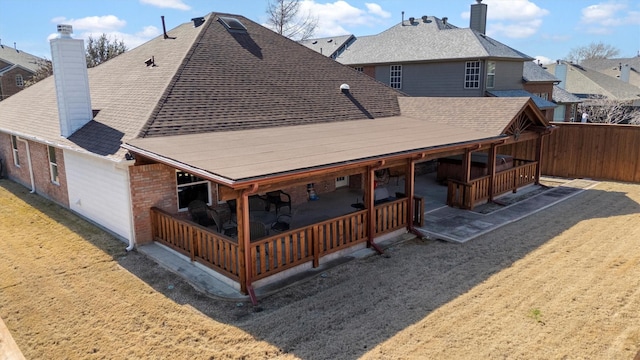 rear view of property with roof with shingles, a chimney, and a patio area