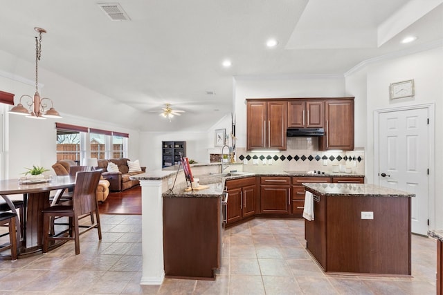 kitchen featuring a kitchen island, ceiling fan with notable chandelier, decorative light fixtures, sink, and backsplash