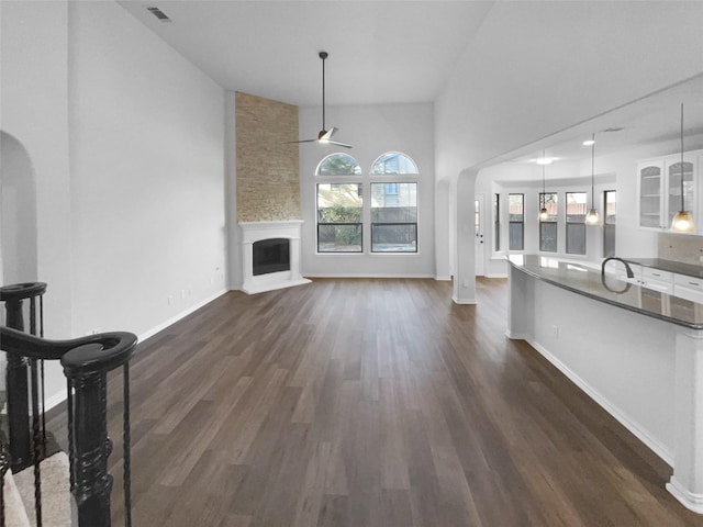 unfurnished living room featuring dark wood-type flooring, sink, a large fireplace, ceiling fan, and a high ceiling