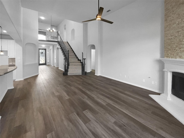 unfurnished living room featuring a towering ceiling, a stone fireplace, dark wood-type flooring, and ceiling fan with notable chandelier