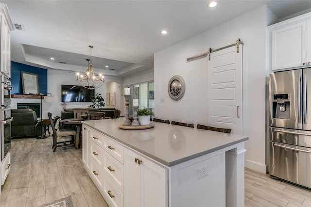 kitchen featuring pendant lighting, appliances with stainless steel finishes, white cabinetry, a center island, and a raised ceiling