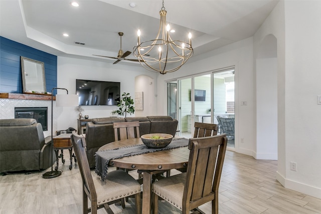 dining area with a raised ceiling, an inviting chandelier, and light hardwood / wood-style flooring