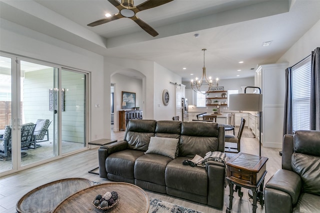 living room featuring ceiling fan with notable chandelier, light hardwood / wood-style floors, and a tray ceiling