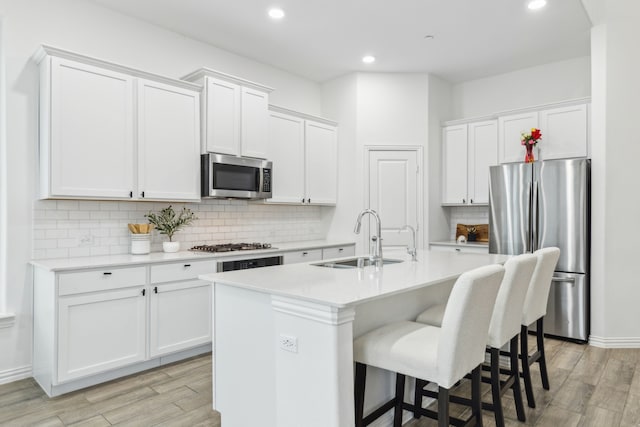 kitchen with sink, light hardwood / wood-style flooring, appliances with stainless steel finishes, a kitchen island with sink, and white cabinets