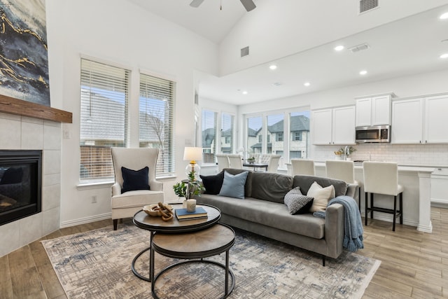 living room featuring ceiling fan, a tiled fireplace, high vaulted ceiling, and light hardwood / wood-style flooring