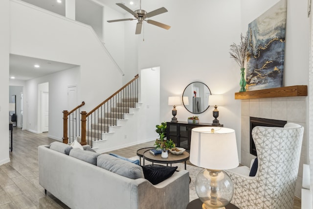 living room featuring ceiling fan, a tiled fireplace, light hardwood / wood-style floors, and a high ceiling