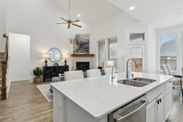 kitchen featuring sink, a tile fireplace, white cabinetry, a center island with sink, and stainless steel dishwasher