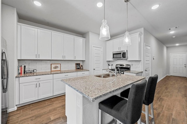 kitchen with sink, white cabinetry, decorative light fixtures, appliances with stainless steel finishes, and a kitchen island with sink