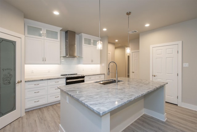 kitchen featuring sink, white cabinets, an island with sink, and wall chimney exhaust hood