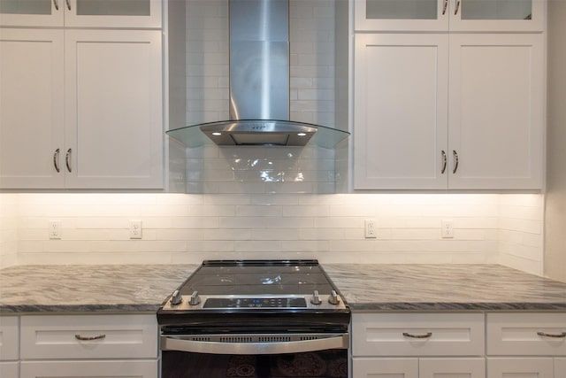 kitchen featuring white cabinetry, light stone counters, electric range, wall chimney range hood, and backsplash