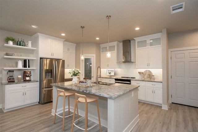 kitchen featuring a kitchen island with sink, white cabinets, wall chimney exhaust hood, and appliances with stainless steel finishes