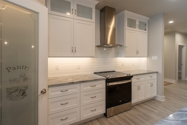 kitchen with white cabinets, stainless steel range with electric stovetop, light hardwood / wood-style floors, and wall chimney exhaust hood