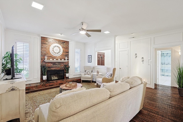 living room featuring ceiling fan, ornamental molding, wood-type flooring, and a brick fireplace