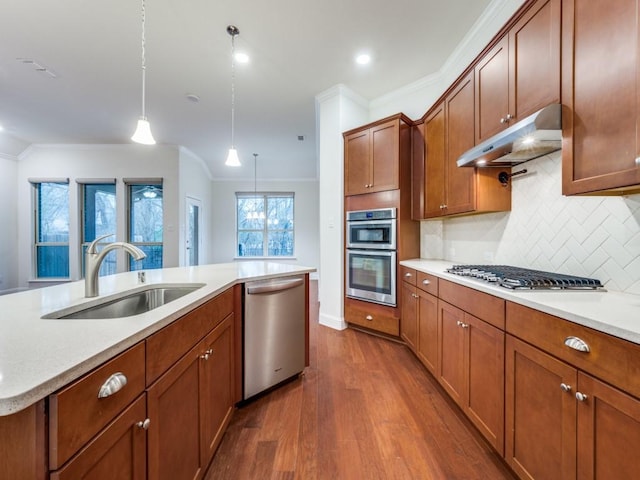 kitchen with sink, a center island with sink, ornamental molding, appliances with stainless steel finishes, and pendant lighting