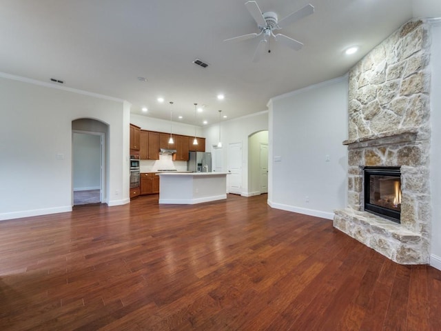 unfurnished living room featuring dark hardwood / wood-style floors, ceiling fan, ornamental molding, and a stone fireplace