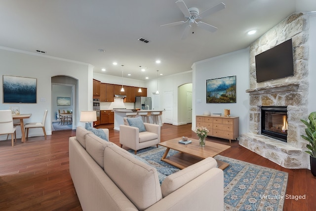 living room featuring ceiling fan, a fireplace, ornamental molding, and dark hardwood / wood-style floors